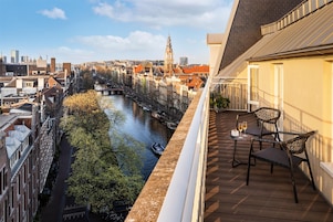 A balcony with a view of a river, historic buildings, and a tower in the distance.