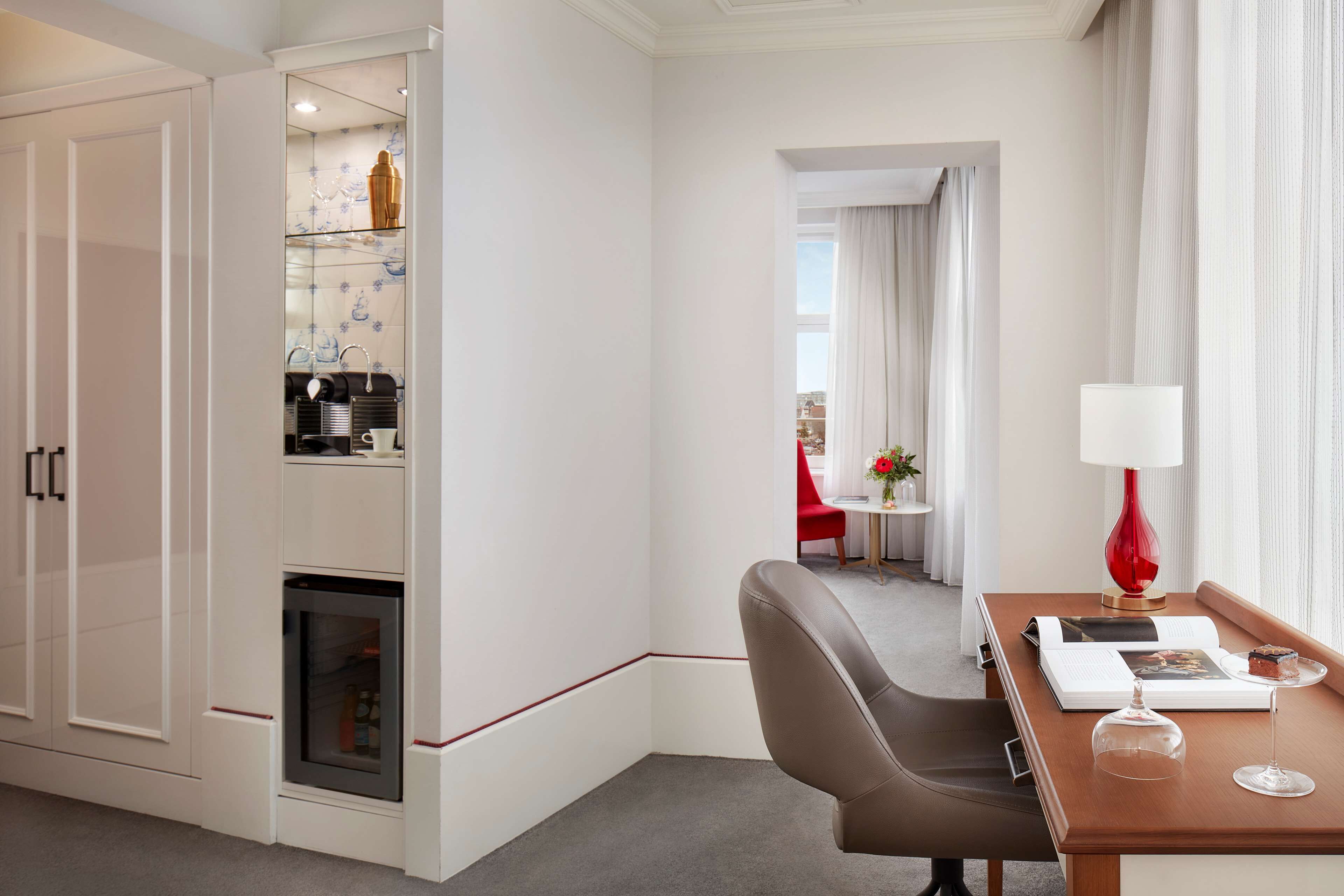 Habitación de hotel con comedor, una silla roja, una mesa con lámpara y vista a la ciudad.