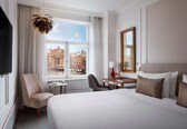 A hotel room with a bed, a desk, a chair, a TV, and a window with a city view.