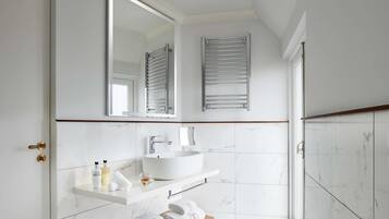 A bathroom with a white sink, mirror, towel rack, and a shower area.