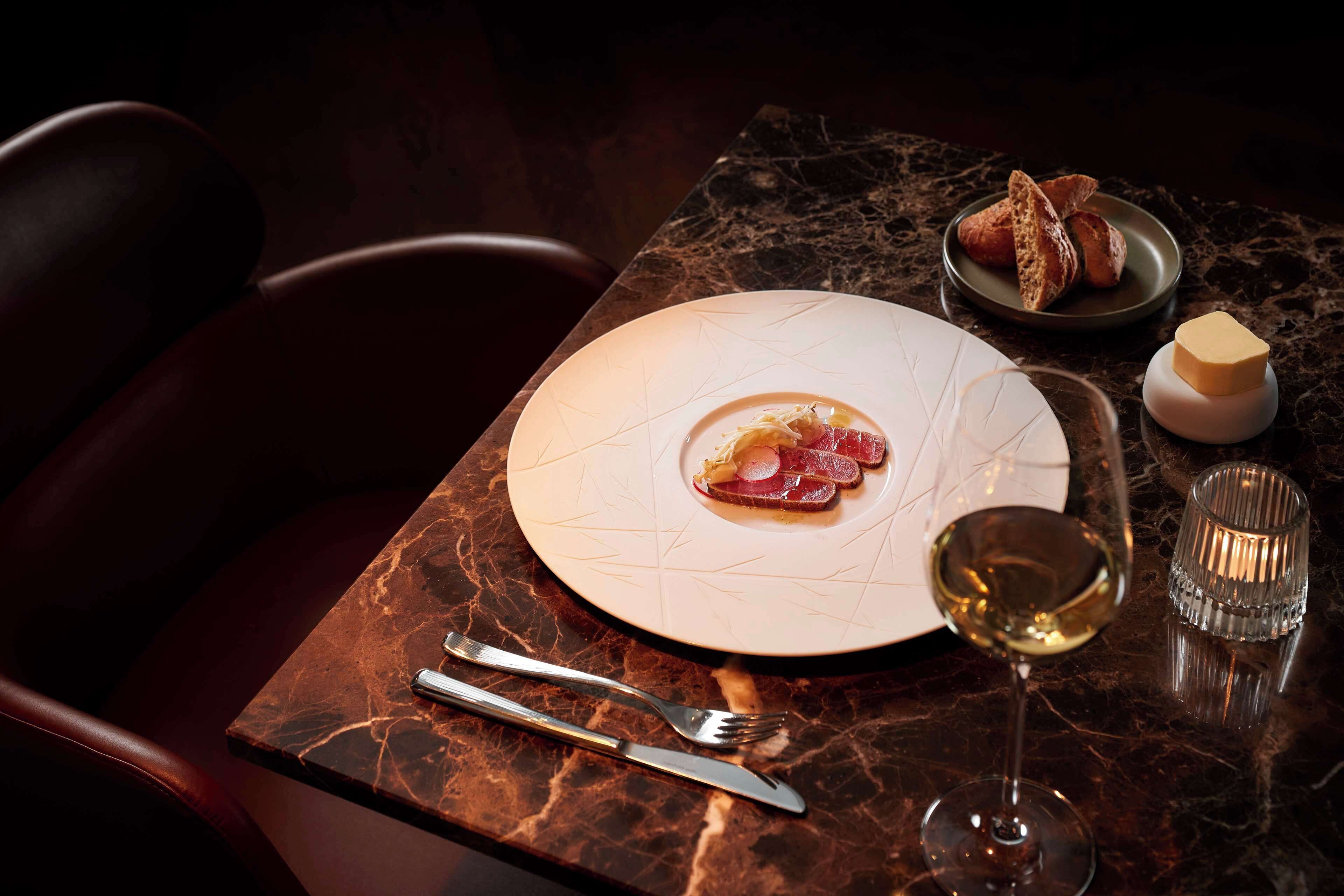 A dining table with a plate of food, a glass of wine, and cutlery.