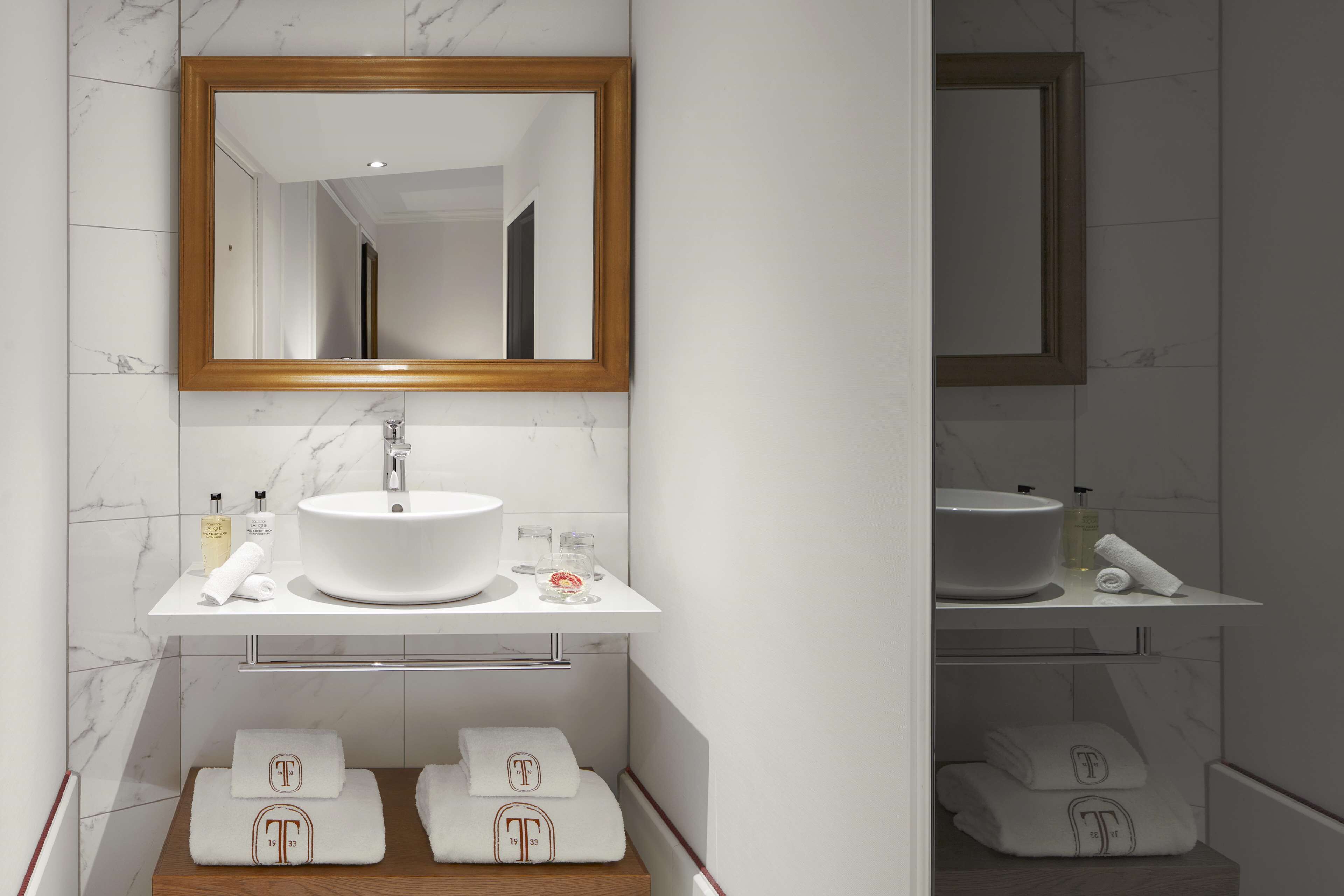 A bathroom with a white sink, mirror, and marble tiles. There are towels and toiletries on the counter.