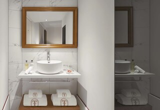 A bathroom with a white sink, mirror, and marble tiles. There are towels and toiletries on the counter.