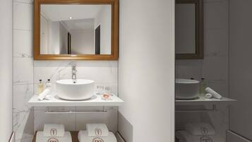A bathroom with a white sink, mirror, and marble tiles. There are towels and toiletries on the counter.