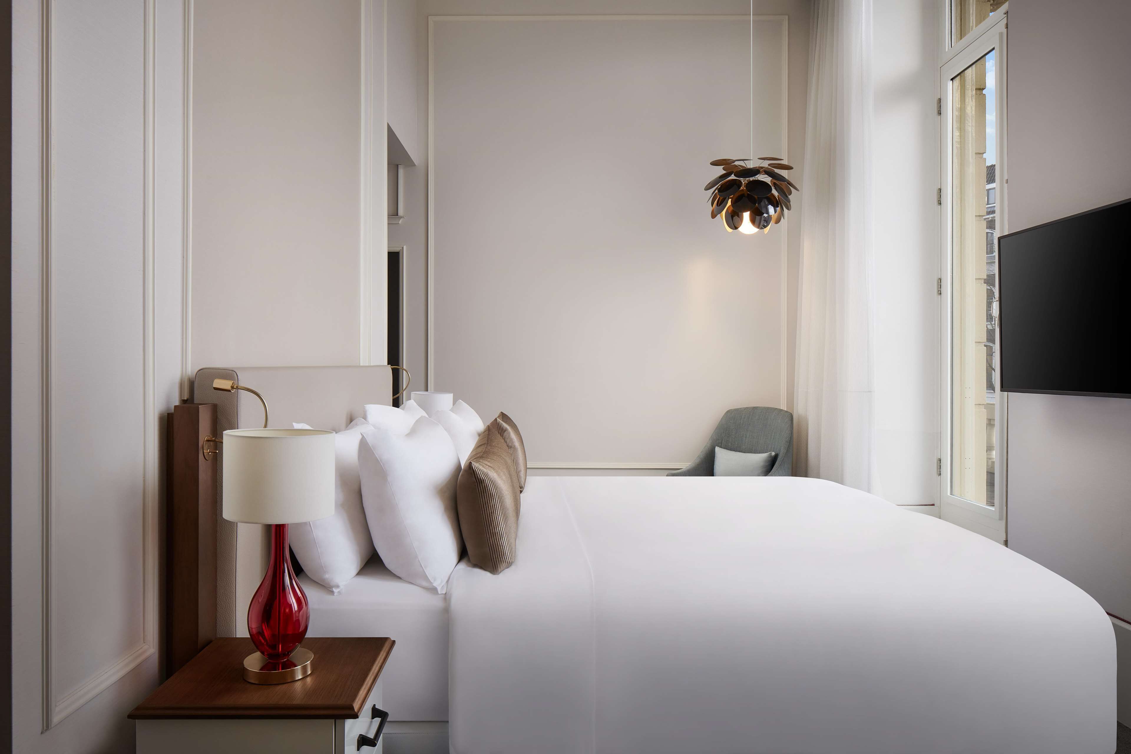 Una habitación de hotel con una cama, una lámpara roja, un televisor y una ventana.