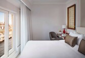 A hotel room with a large bed, a chair, a desk with a lamp, a framed picture, and a view through a window.