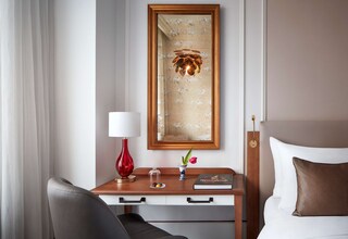 A hotel room with a bed, a bedside table with a lamp, a vase with a flower, a framed picture, and a book.