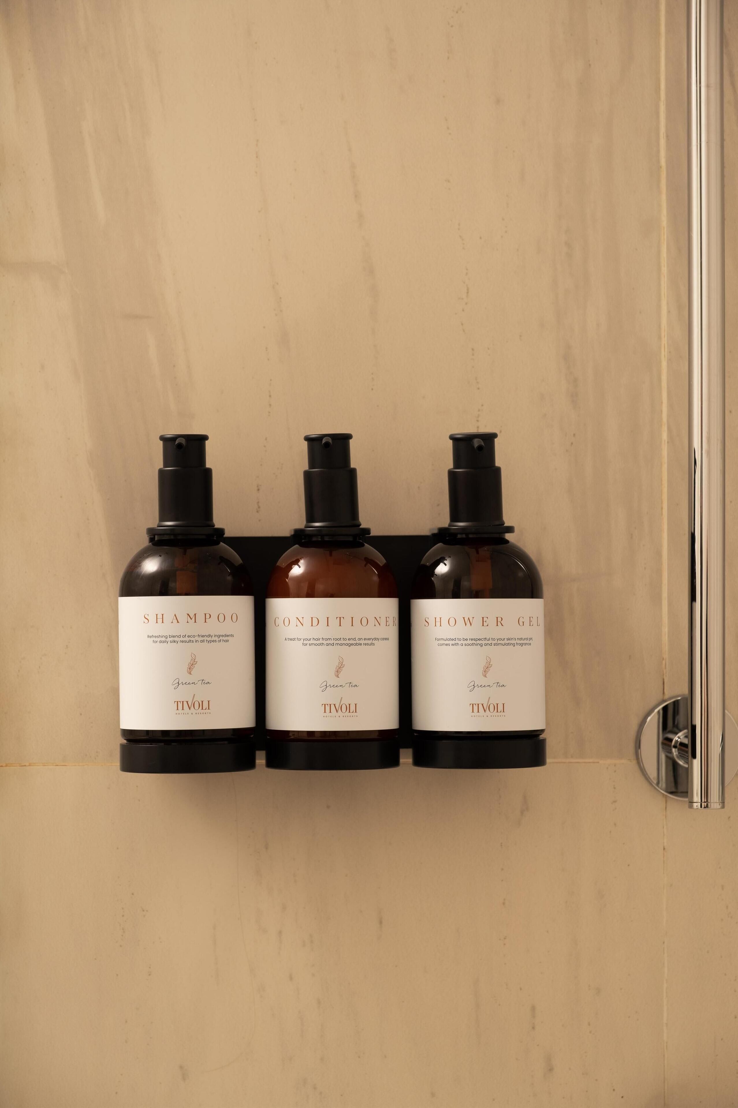 Trois bouteilles de produits de soins capillaires au thé vert sont posées sur un mur.