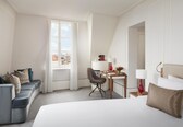 A hotel room with a bed, a desk, a chair, a sofa, a window with curtains, and a city view.