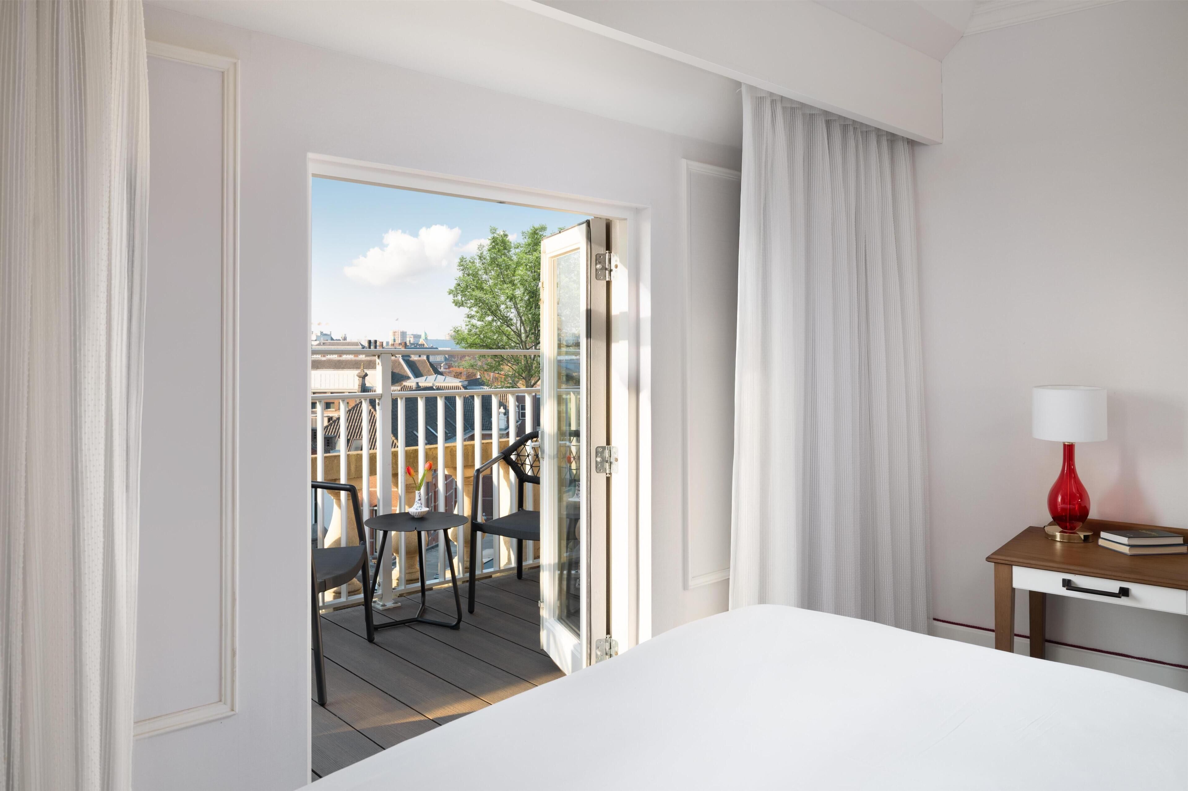 Een hotelkamer met balkon, een bed, bureau met lamp en uitzicht op de stad.