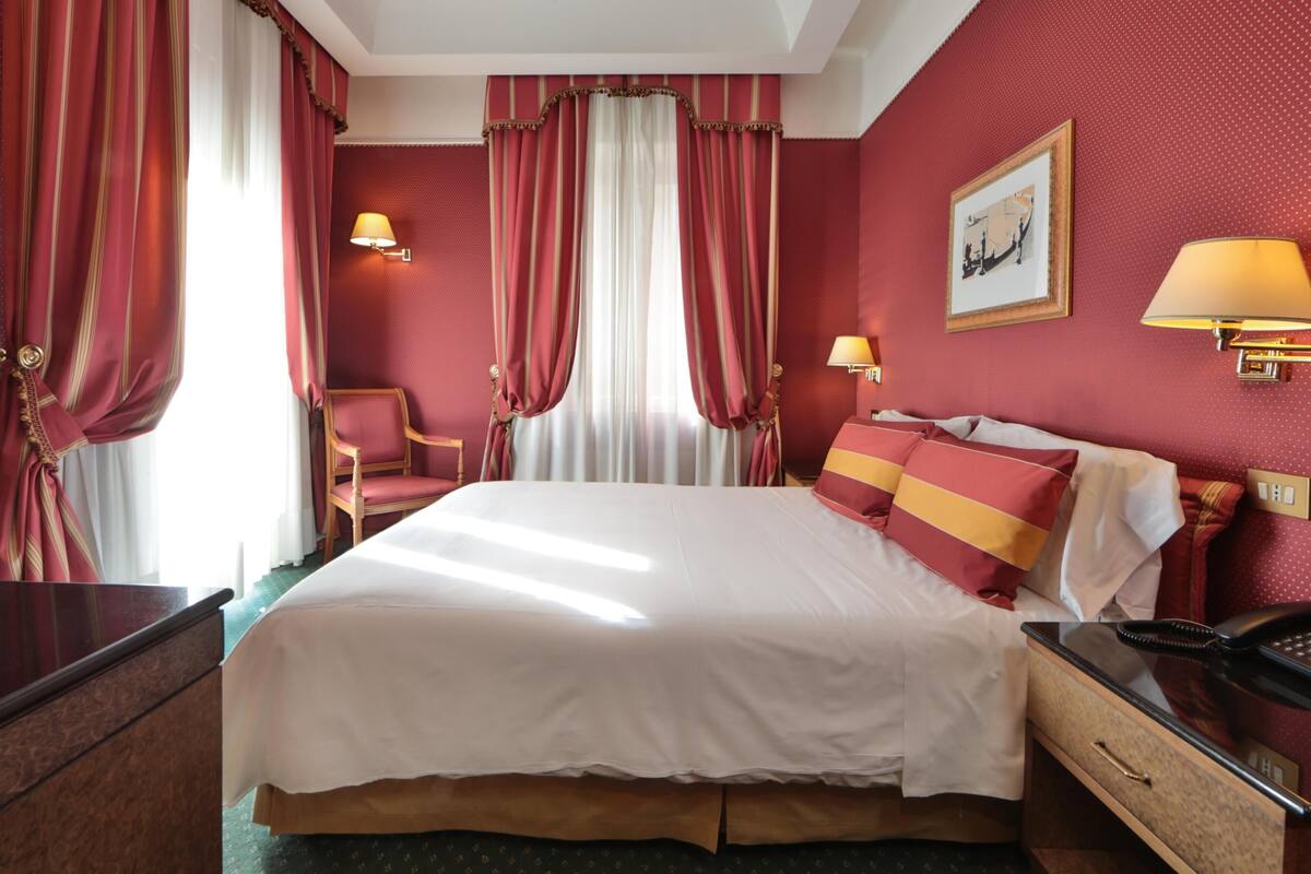 A hotel room with a large bed, two bedside lamps, a chair, a desk, and a telephone.