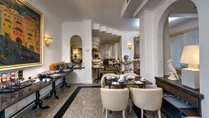 A hotel lobby with a long reception counter, a large painting, and a chandelier. There are tables and chairs set up for dining, and a buffet area with various food items. - Best Western Hotel Rivoli (Rome)
