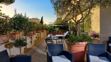 Eine Terrasse im Freien mit Korbmöbeln, Blumentöpfen und einer Sitzecke mit Blick auf die Stadtlandschaft.