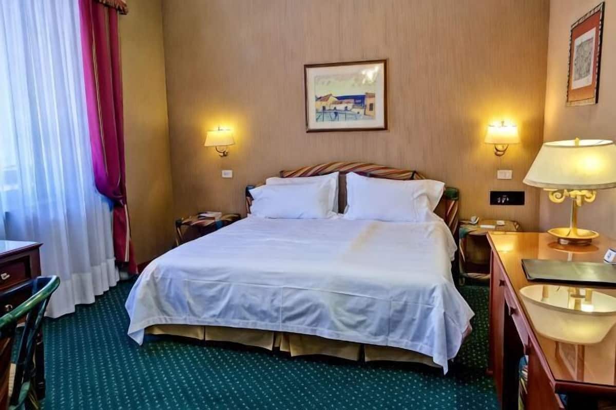 A hotel room with a bed, two bedside lamps, a nightstand, a desk, and a chair.