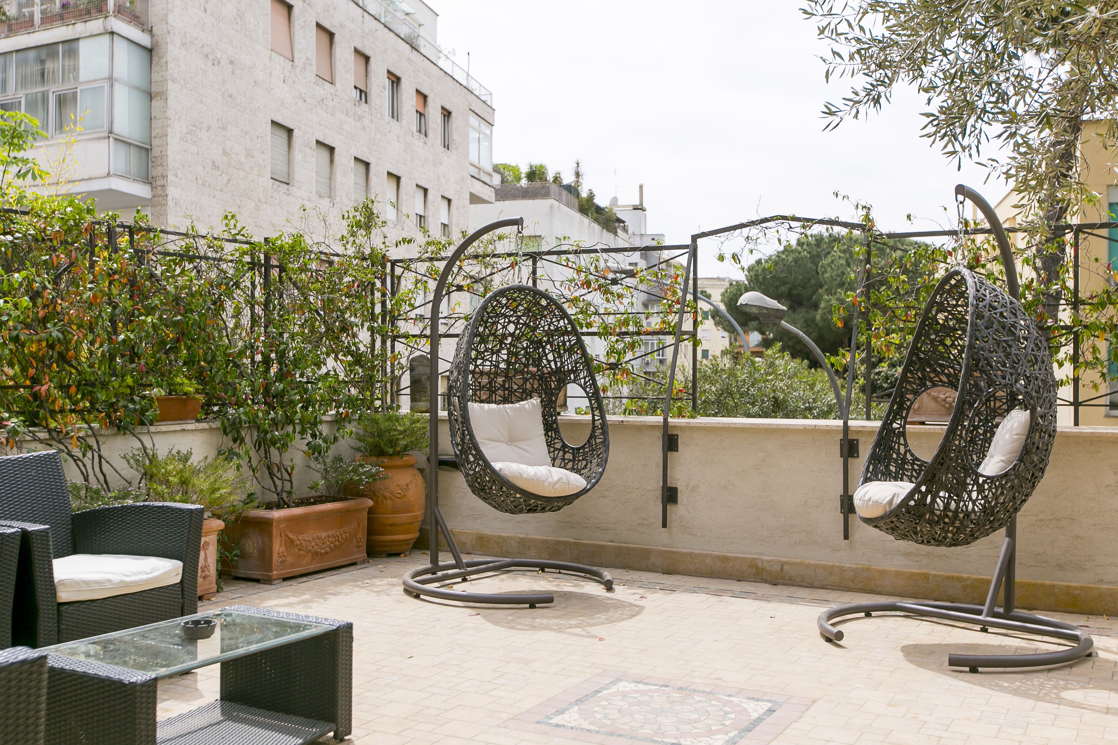 Una terrazza sul tetto con mobili in vimini, poltrone sospese e piante in vaso.