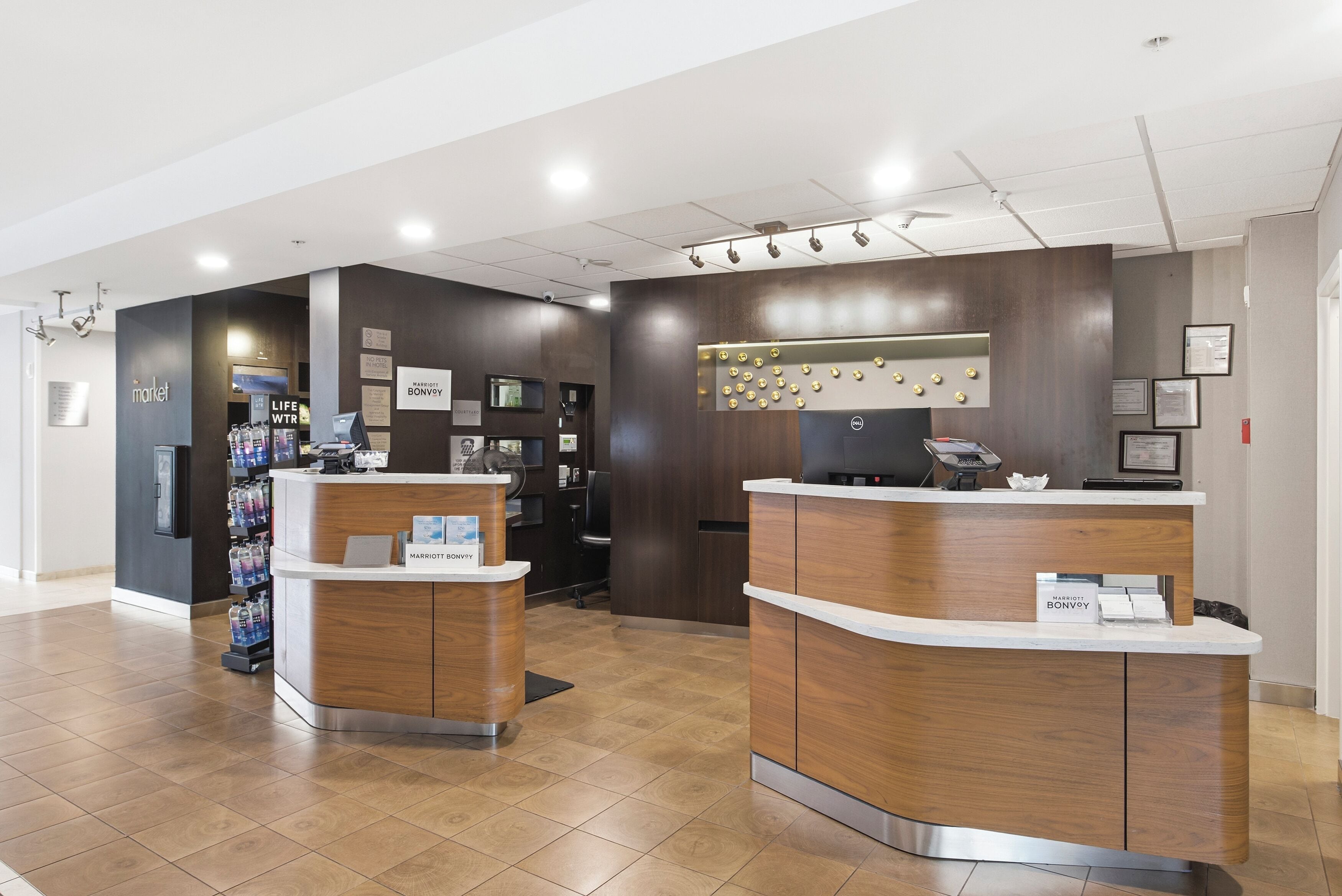 A hotel reception area with two wooden reception desks, a digital screen, and a wall-mounted information board.