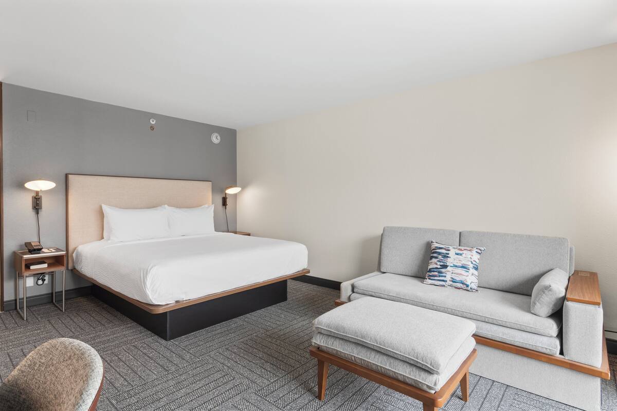 A hotel room with a bed, a sofa, a chair, and a small table.