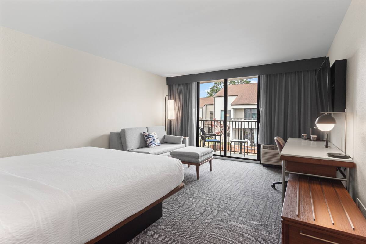 A hotel room with a large bed, a desk, a chair, a sofa, and a view of the outside.
