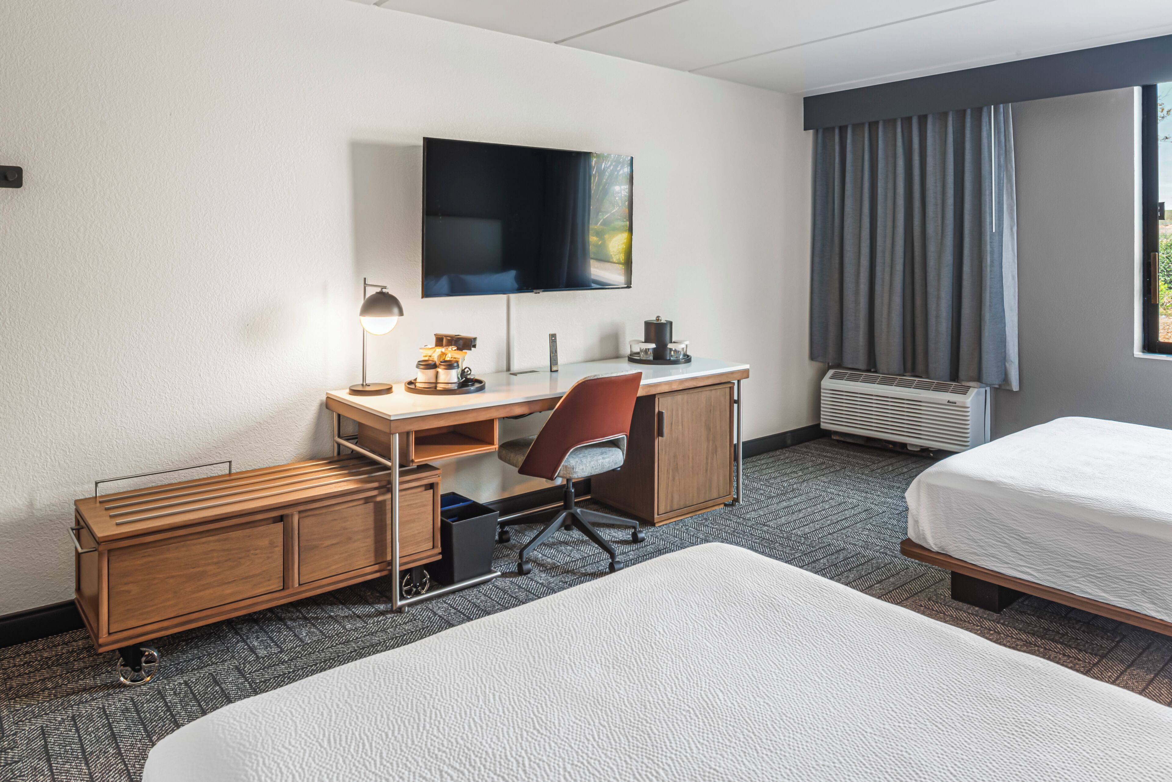 Ein Hotelzimmer mit einem Bett, einem Schreibtisch mit Stuhl, einem Fernseher und einem Fenster mit Vorhängen.