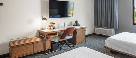 Ein Hotelzimmer mit einem Bett, einem Schreibtisch mit Stuhl, einem Fernseher und einem Fenster mit Vorhängen.