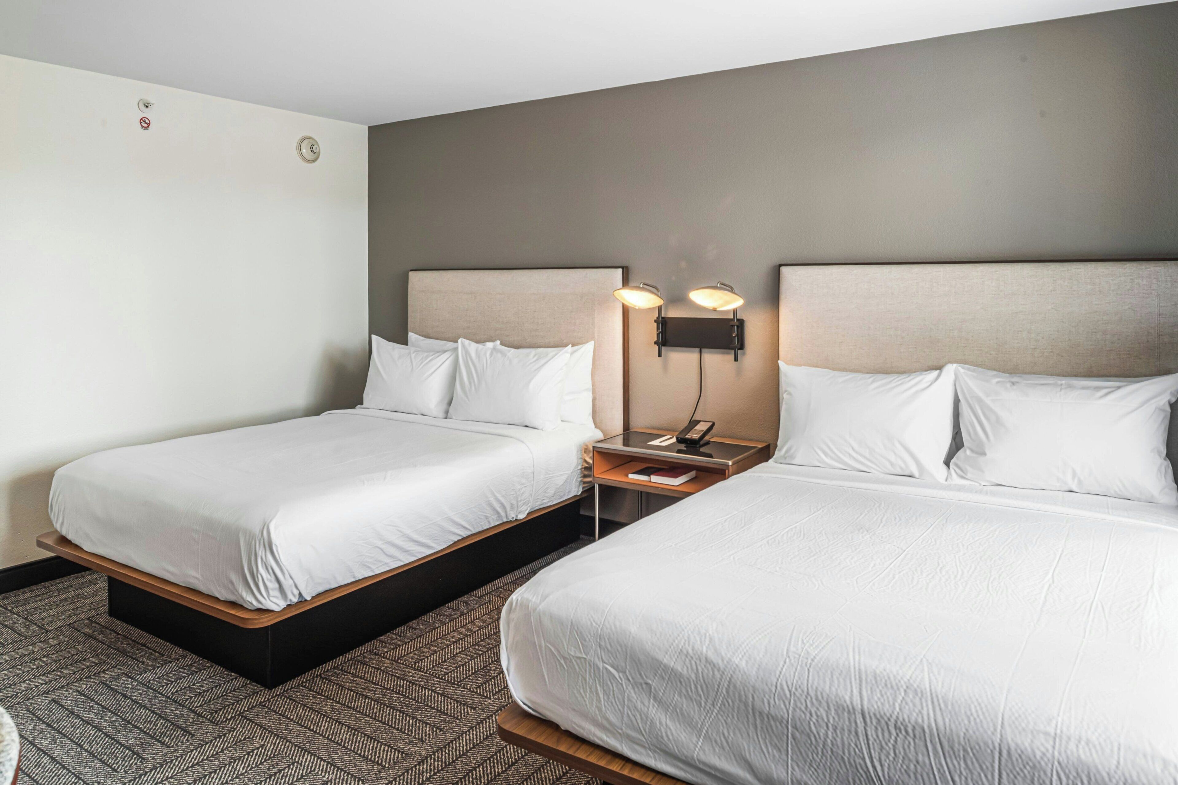Een hotelkamer met twee bedden, een nachtkastje met een lamp en een wandlamp.