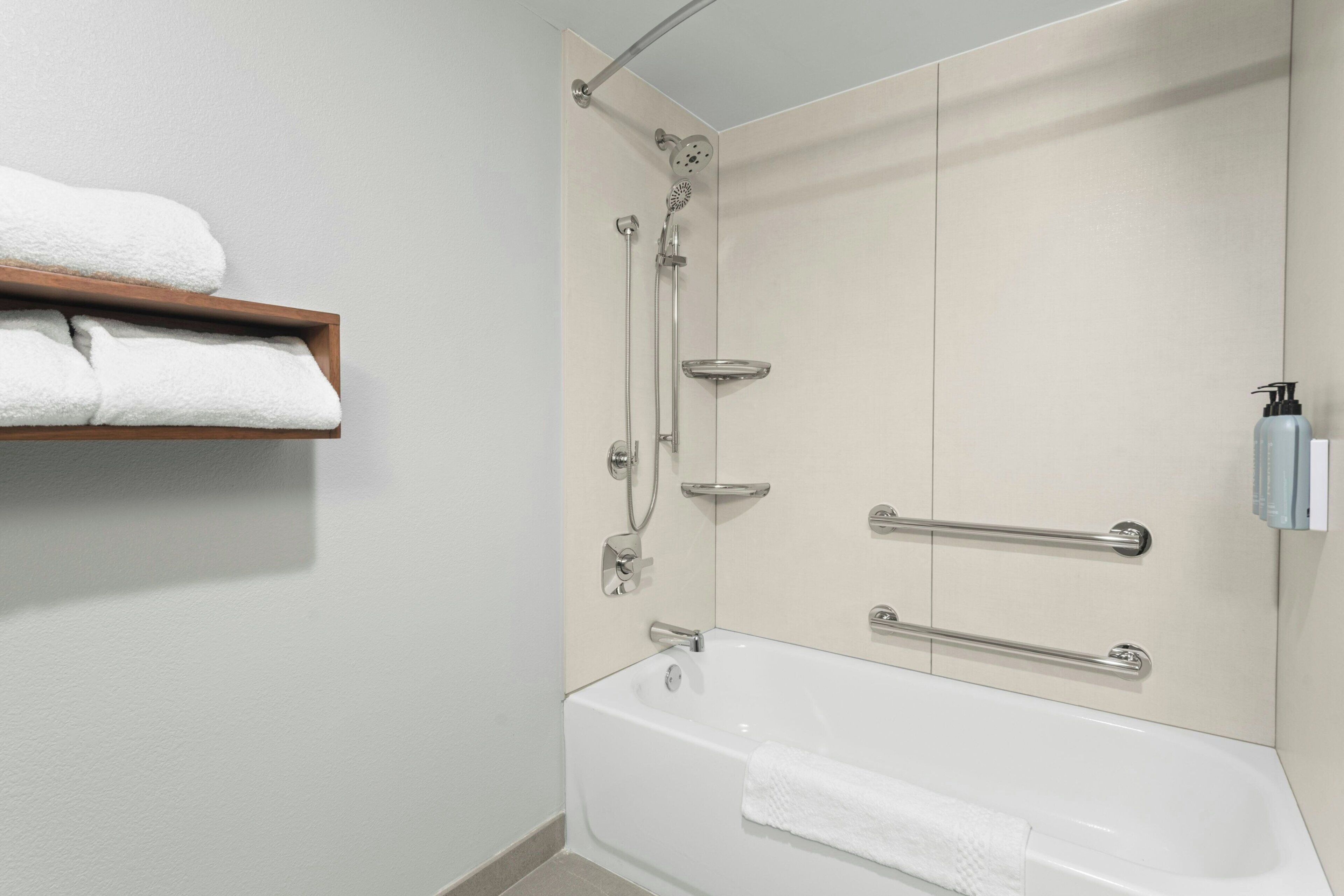 Une salle de bain moderne avec une baignoire, une douche et une étagère où sont rangées les serviettes.