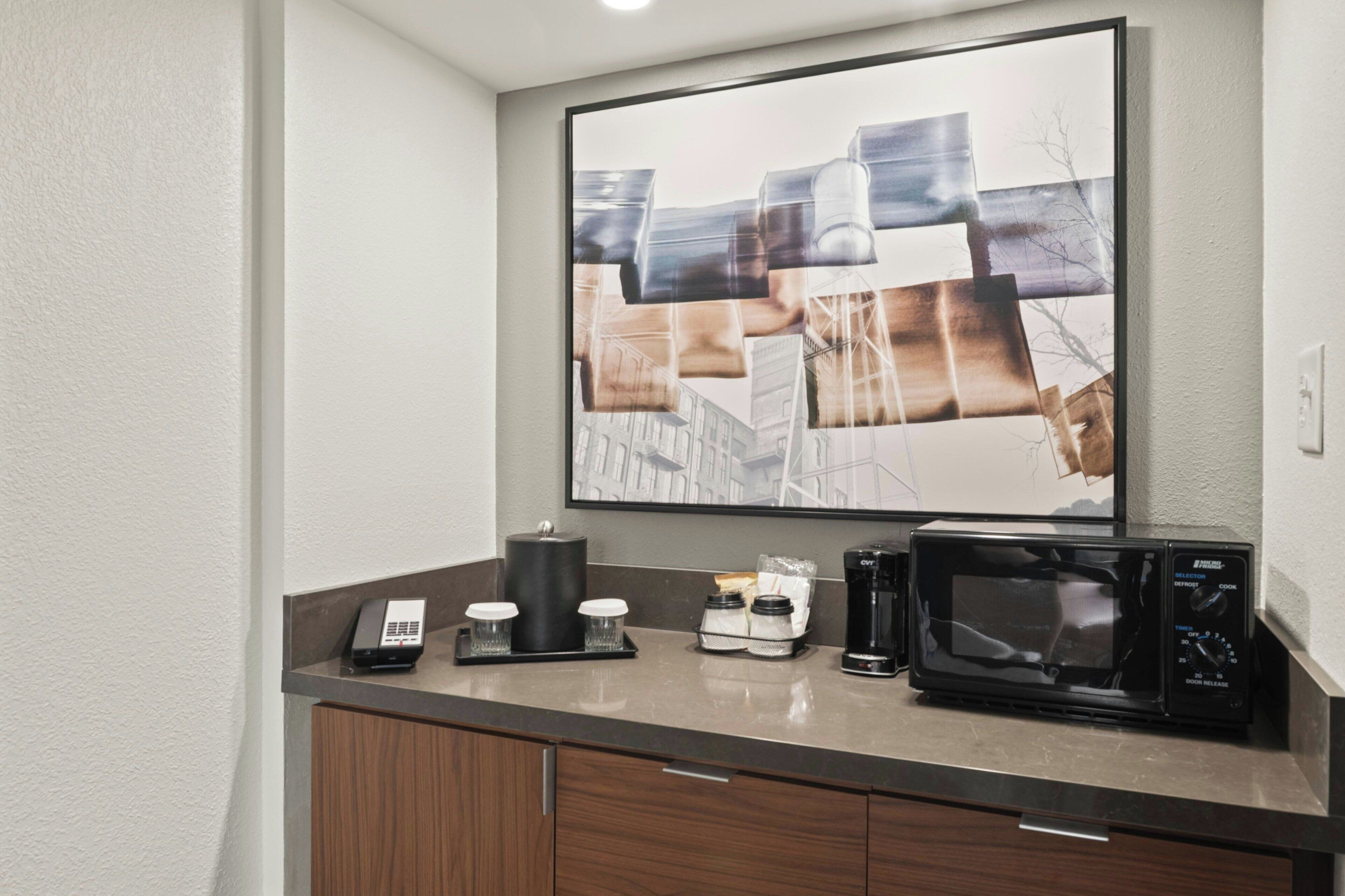 A hotel kitchenette with a coffee maker, microwave, and a phone on the counter.