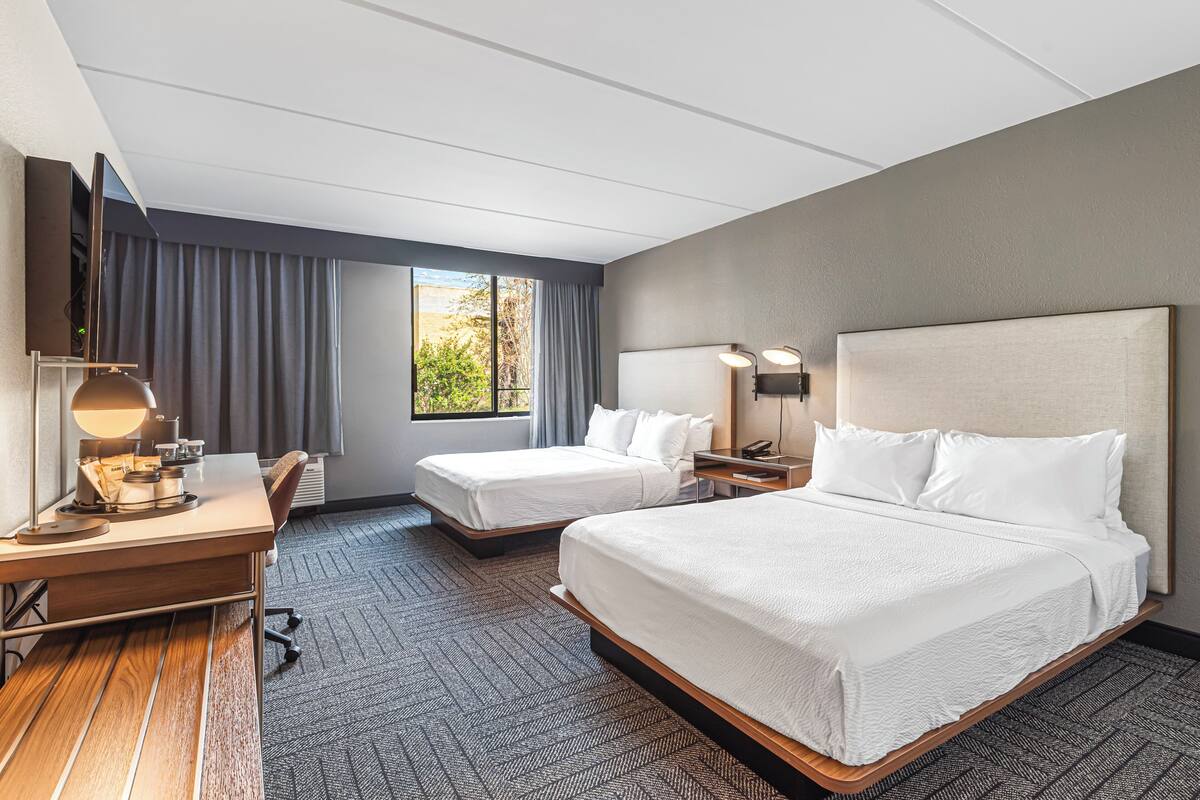 A hotel room with two beds, a desk, a TV, and a window with curtains.