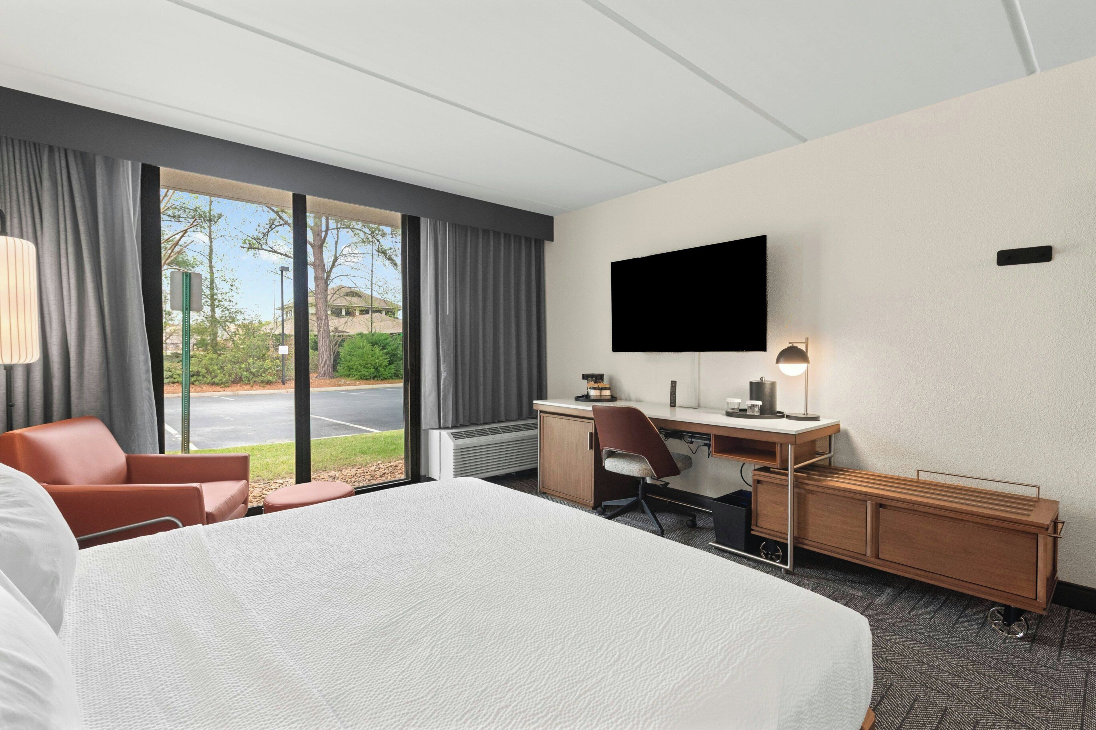 A hotel room with a bed, desk, chair, TV, and a view of the outdoors.