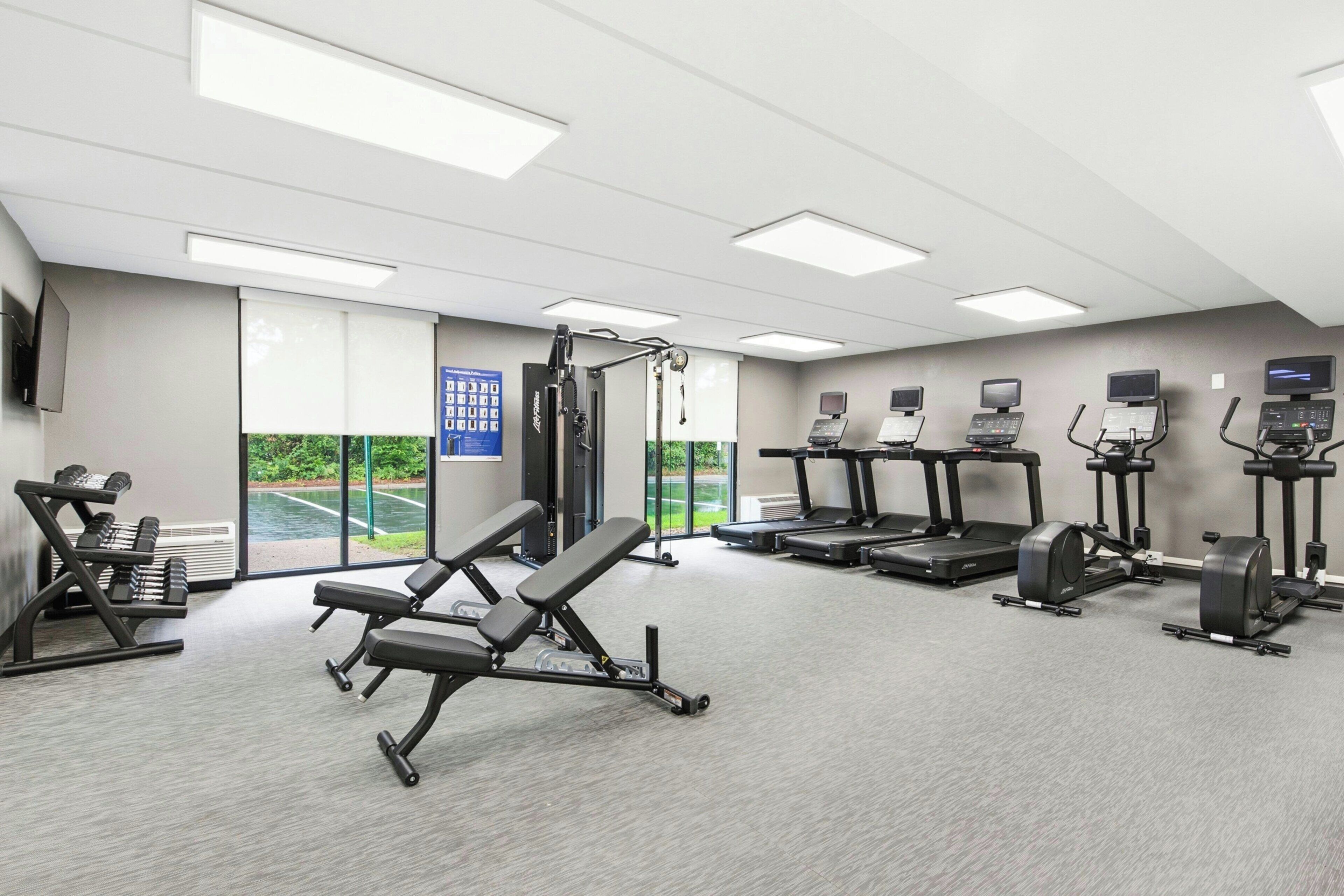 Une salle de sport équipée de divers appareils d’exercice, notamment des tapis de course, un banc de développé couché et des haltères.