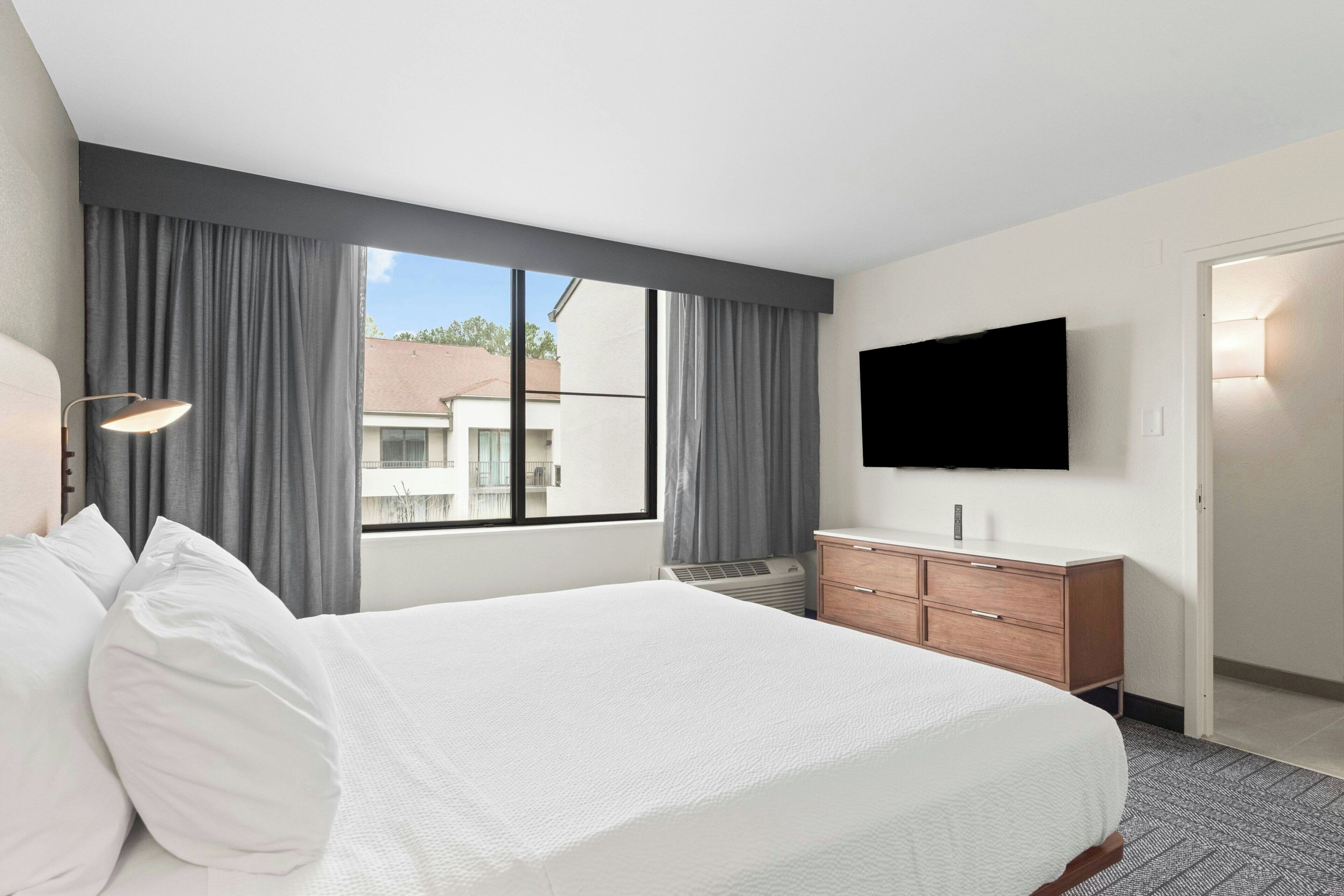 A hotel room with a large bed, a flat-screen TV, a dresser, and a window with curtains.