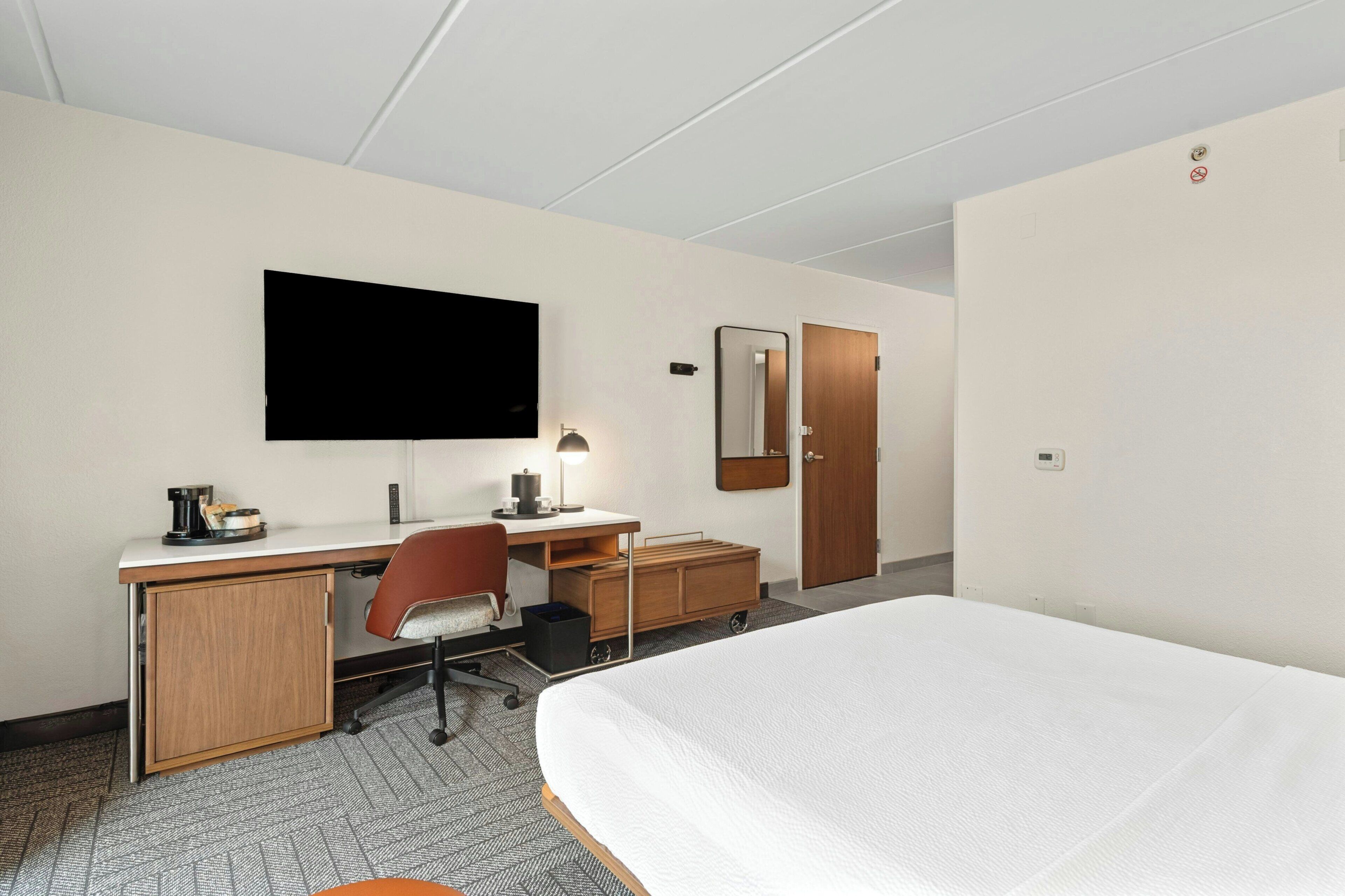 A hotel room with a bed, desk, chair, TV, and a wardrobe.