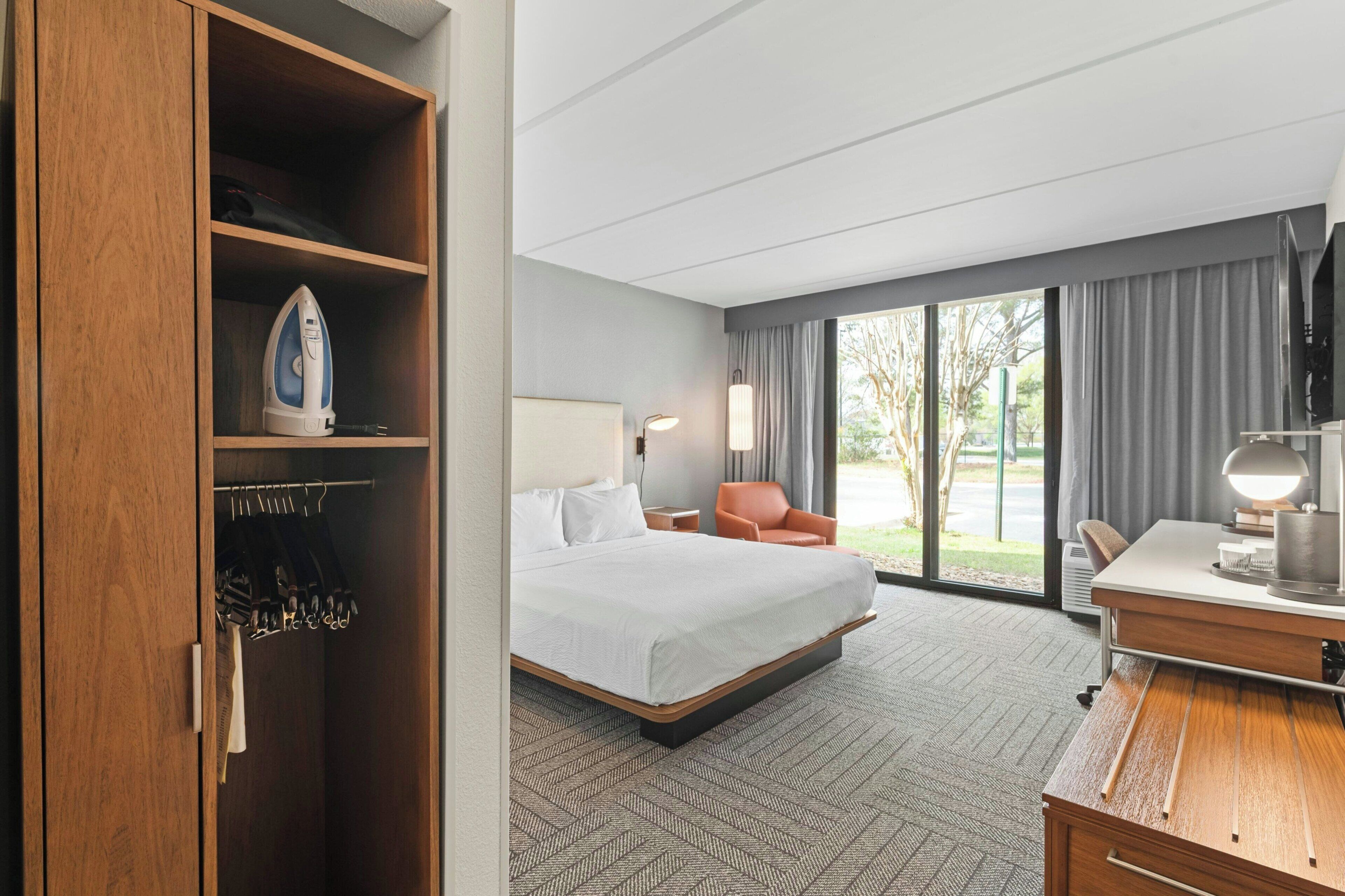 Habitación de hotel con cama, escritorio, silla, armario y vistas al exterior.