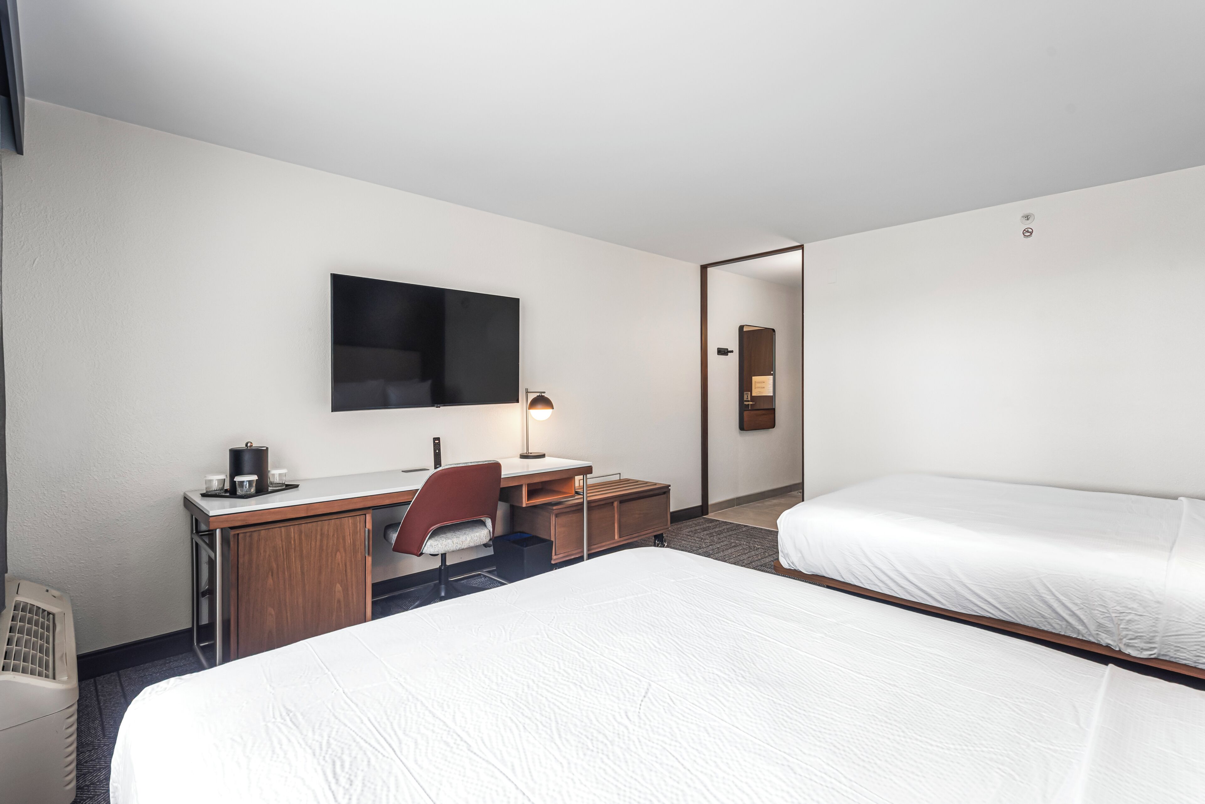 Una habitación de hotel con cama, escritorio, silla, televisor y espejo.