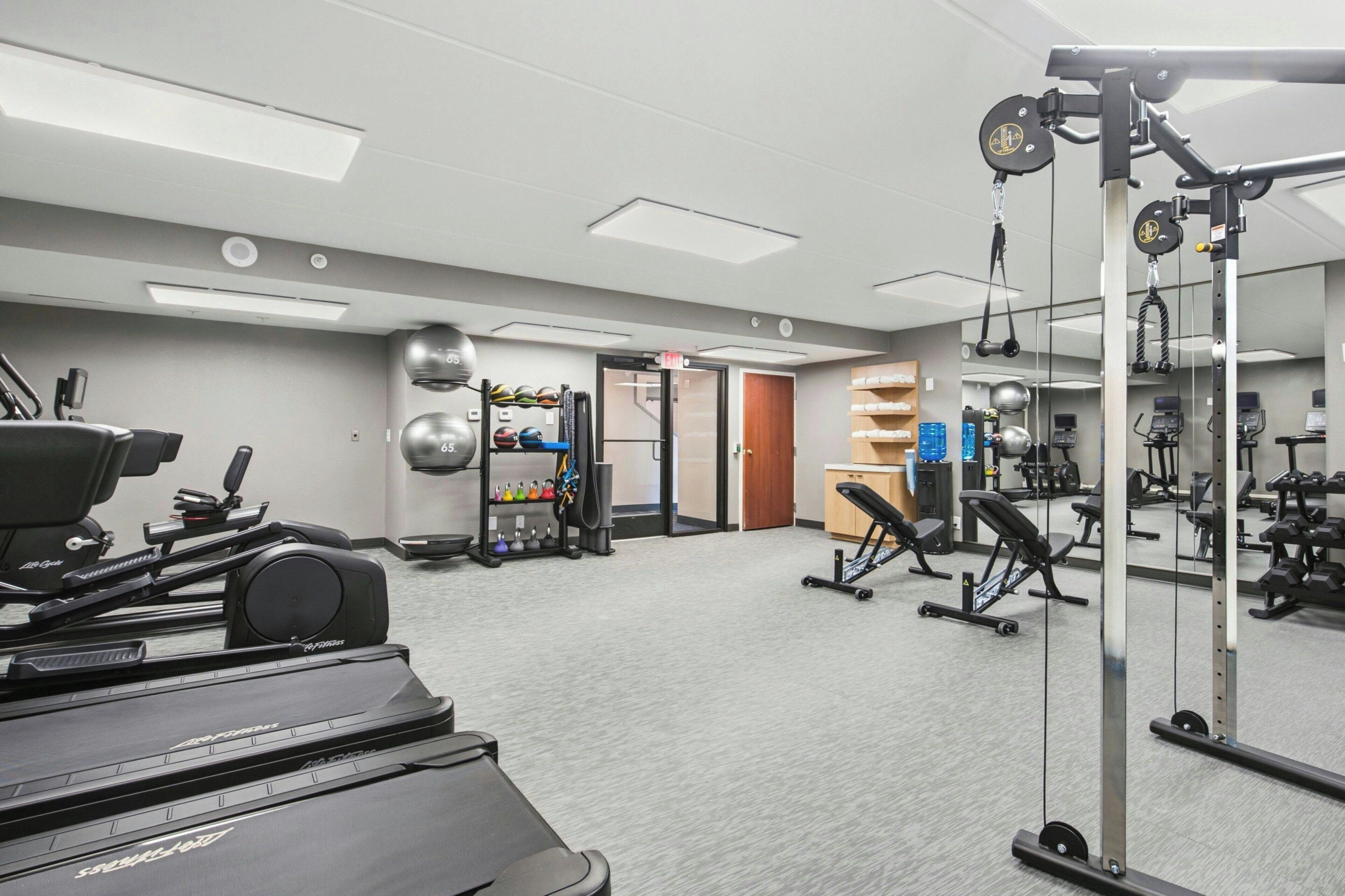 A gym with cardio equipment, weightlifting stations, and a mirror.