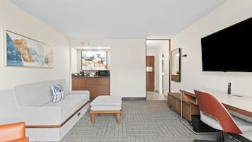 Een hotelkamer met een bank, voetenbankje, bureau, stoel, kitchenette en een aan de muur bevestigde televisie.