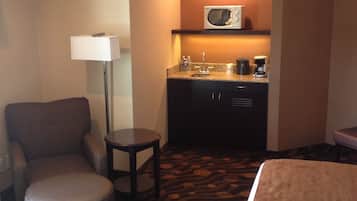 A hotel room with a bed, a chair, a small table, a microwave, and a kitchenette.