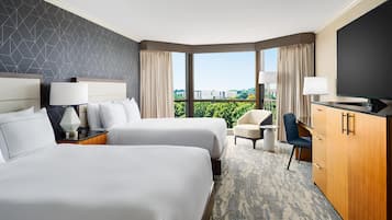 Une chambre d’hôtel avec deux lits, un bureau, une chaise, une télévision et une grande fenêtre donnant sur la ville.