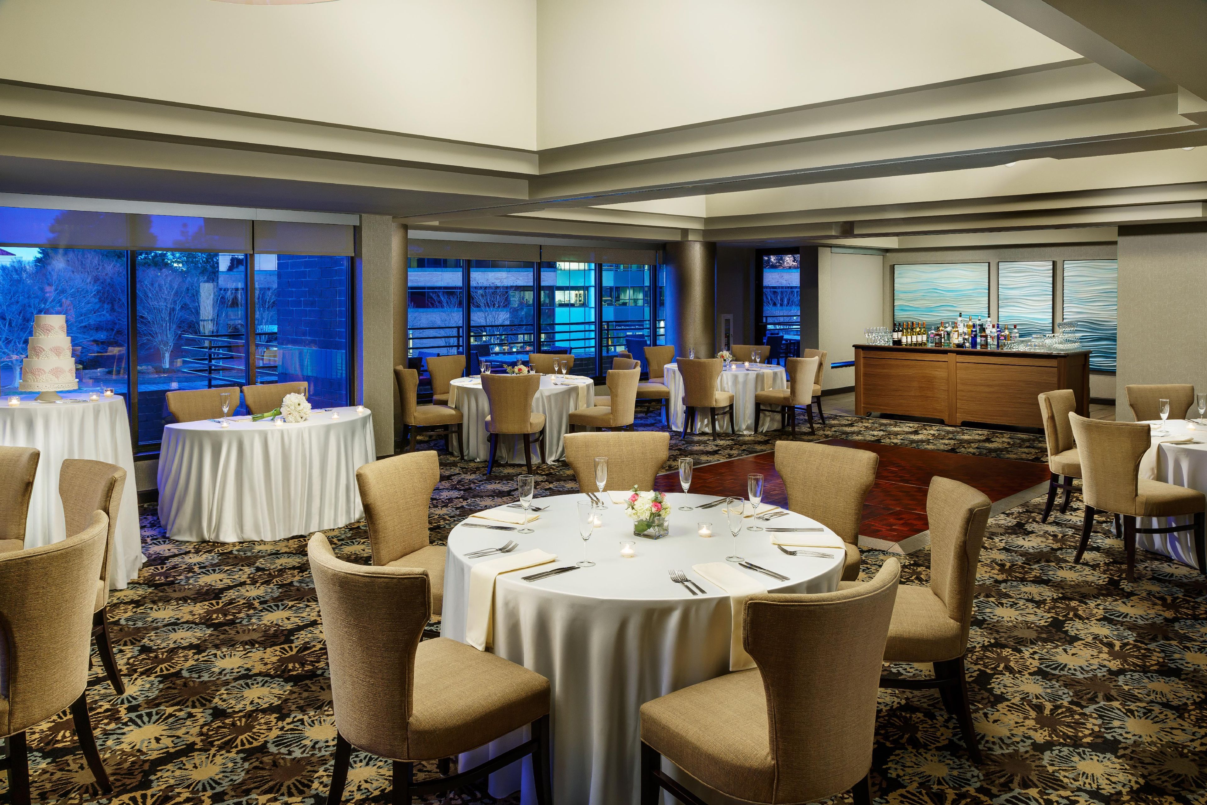 A hotel dining area with round tables, chairs, and a bar.