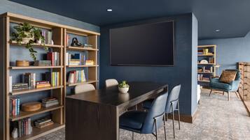 A modern living room with a dark wooden dining table, blue chairs, and a large bookshelf filled with books and decorative items.