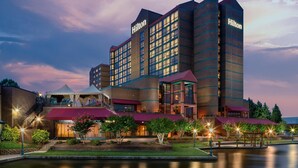 A multi-story hotel with a prominent 'Hilton' sign, a landscaped courtyard, and a body of water in front. - Hilton Charlotte University Place (Charlotte)