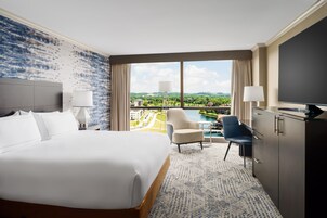 Une chambre d’hôtel avec un grand lit, un bureau, une chaise, une télévision et une vue sur un paysage verdoyant.