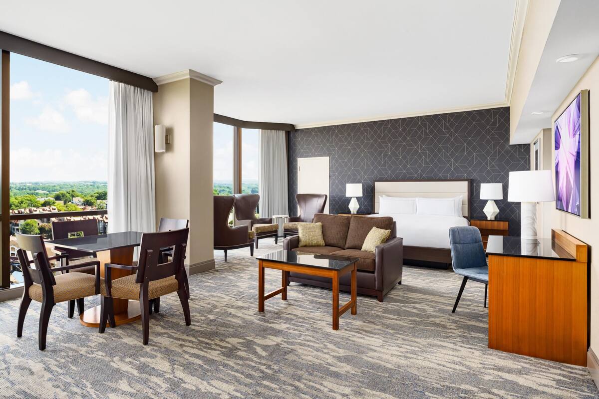 A hotel room with a dining area, a sofa, a bed, and a desk.