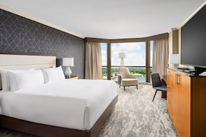 A hotel room with a large bed, a desk, a chair, a TV, and a view of the city.