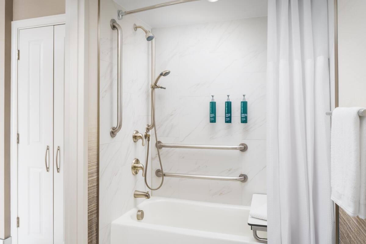 A bathroom with a bathtub, a shower with grab bars, and a set of toiletries on the wall.