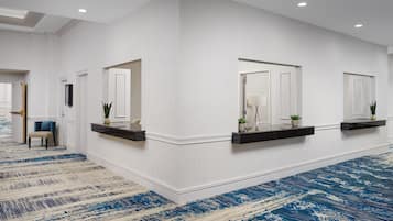 Una hall d'albergo con una lunga reception, due specchi, un tappeto azzurro a motivi decorativi e una sedia.