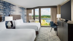 A hotel room with two beds, a desk, a TV, and a large window with a view of a body of water and greenery. - Hilton Charlotte University Place (Charlotte)