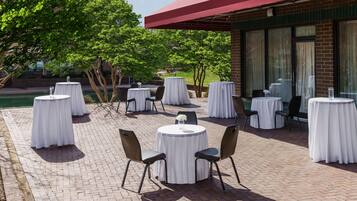 Outdoor round tables with chairs, a brick patio, and a building with a red awning in the background.