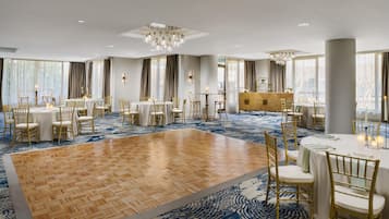 Un amplio salón de banquetes con varias mesas redondas, sillas doradas y una plataforma de madera en el centro.
