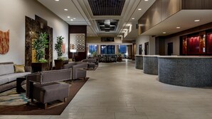A hotel lobby with a reception desk, seating area, and large windows. - Hilton Charlotte University Place (Charlotte)